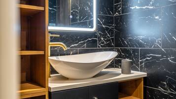 A bathroom with a white vessel sink, a mirror, and black marble walls.