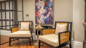 A modern living room with two wicker chairs, a painting on the wall, and a small table with books.