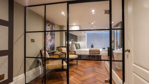 A modern bedroom with a wooden herringbone floor, a glass partition, and a large painting on the wall.