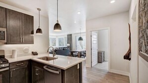 A modern kitchen with dark cabinets, a central island, stainless steel appliances, and pendant lighting. - Clearwater Lofts Luxury 1 Bed Condo Near Lakeside Village (Keystone)