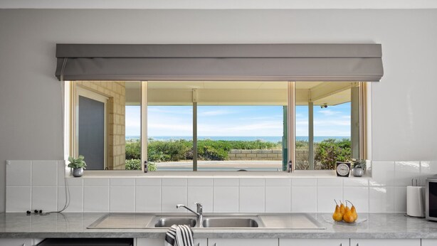 A kitchen with a large window overlooking a scenic view, a sink, and a countertop with a few items. - The Dunes *Pet Friendly* Sea Retreat Busselton (Wonnerup)