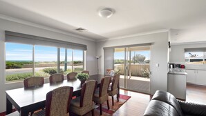 A spacious living area with a dining table and chairs, a sofa, and large windows offering a view of the outdoors. - The Dunes *Pet Friendly* Sea Retreat Busselton (Wonnerup)