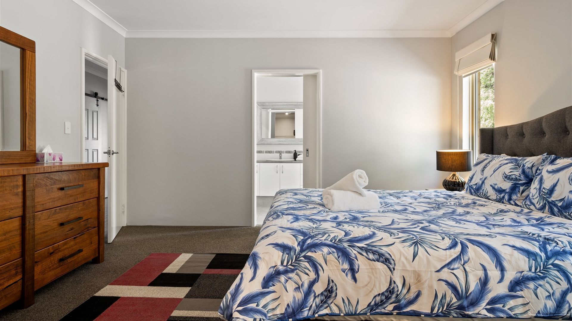 A bedroom with a bed, a dresser, a mirror, and a window.