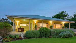 A two-story house with a covered porch, a dining area with a table and chairs, and a well-maintained garden with various plants and shrubs. - The Dunes *Pet Friendly* Sea Retreat Busselton (Wonnerup)