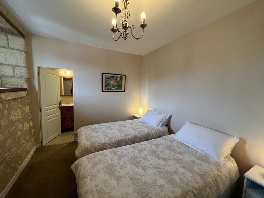 Une chambre avec deux lits, un lustre, un tableau au mur et une salle de bain visible à travers une porte ouverte.