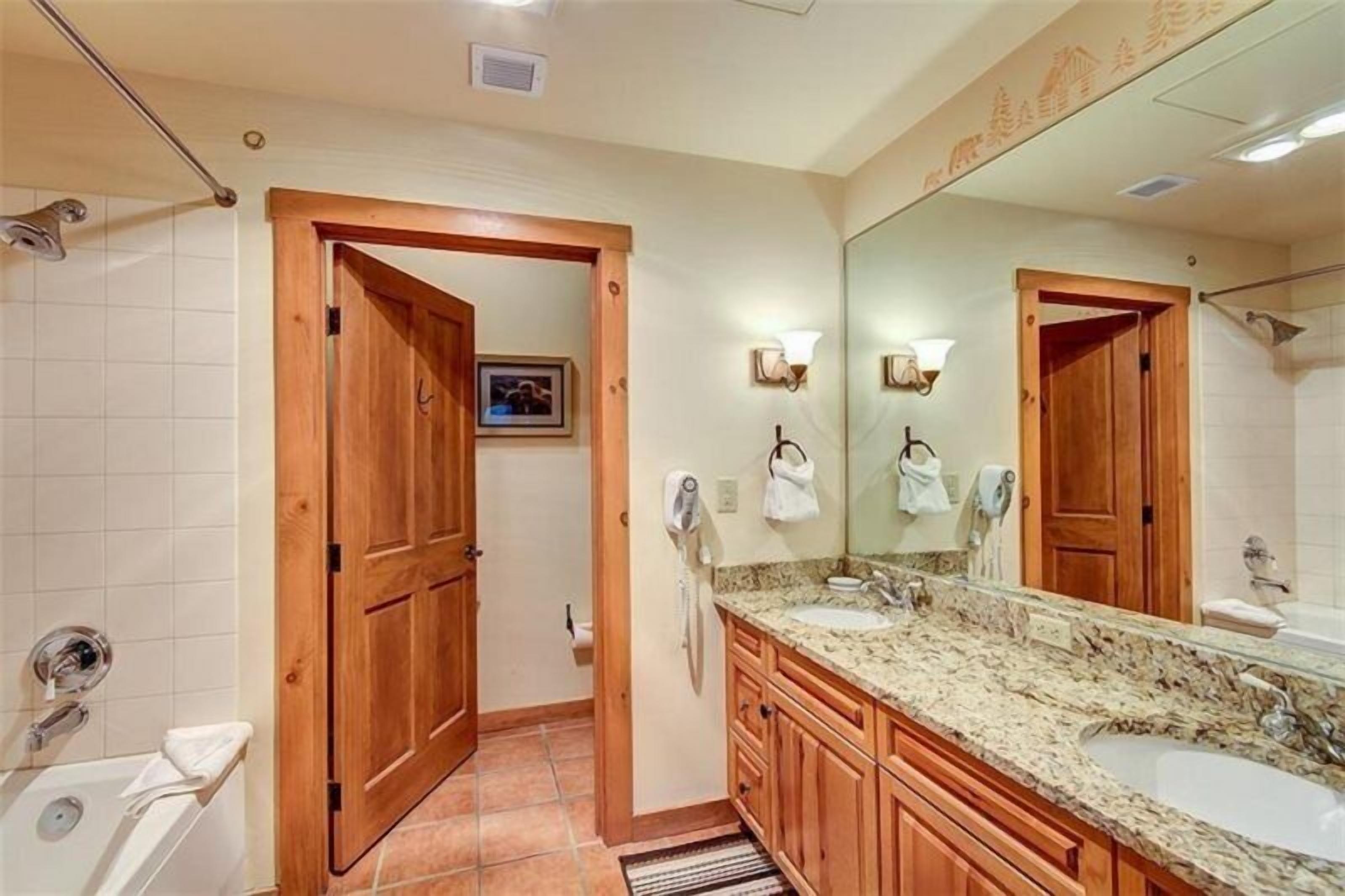 Un baño con puertas de madera, un espejo grande, dos lavamanos y una ducha.