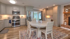 A kitchen with white cabinets, stainless steel appliances, a round dining table with chairs, and a patterned rug. - Discover Sea Glass: a cozy Oak Island retreat with 3 bedrooms and pet-friendly amenities! (Oak Island)