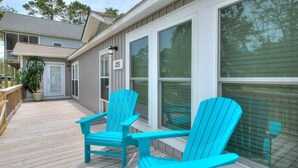A wooden deck with two turquoise Adirondack chairs, a potted plant, and a house with a number 325 sign. - Discover Sea Glass: a cozy Oak Island retreat with 3 bedrooms and pet-friendly amenities! (Oak Island)