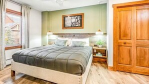Ein Schlafzimmer mit Bett, Nachttischen, Deckenventilator, Holztür und einem Fenster mit Vorhängen.