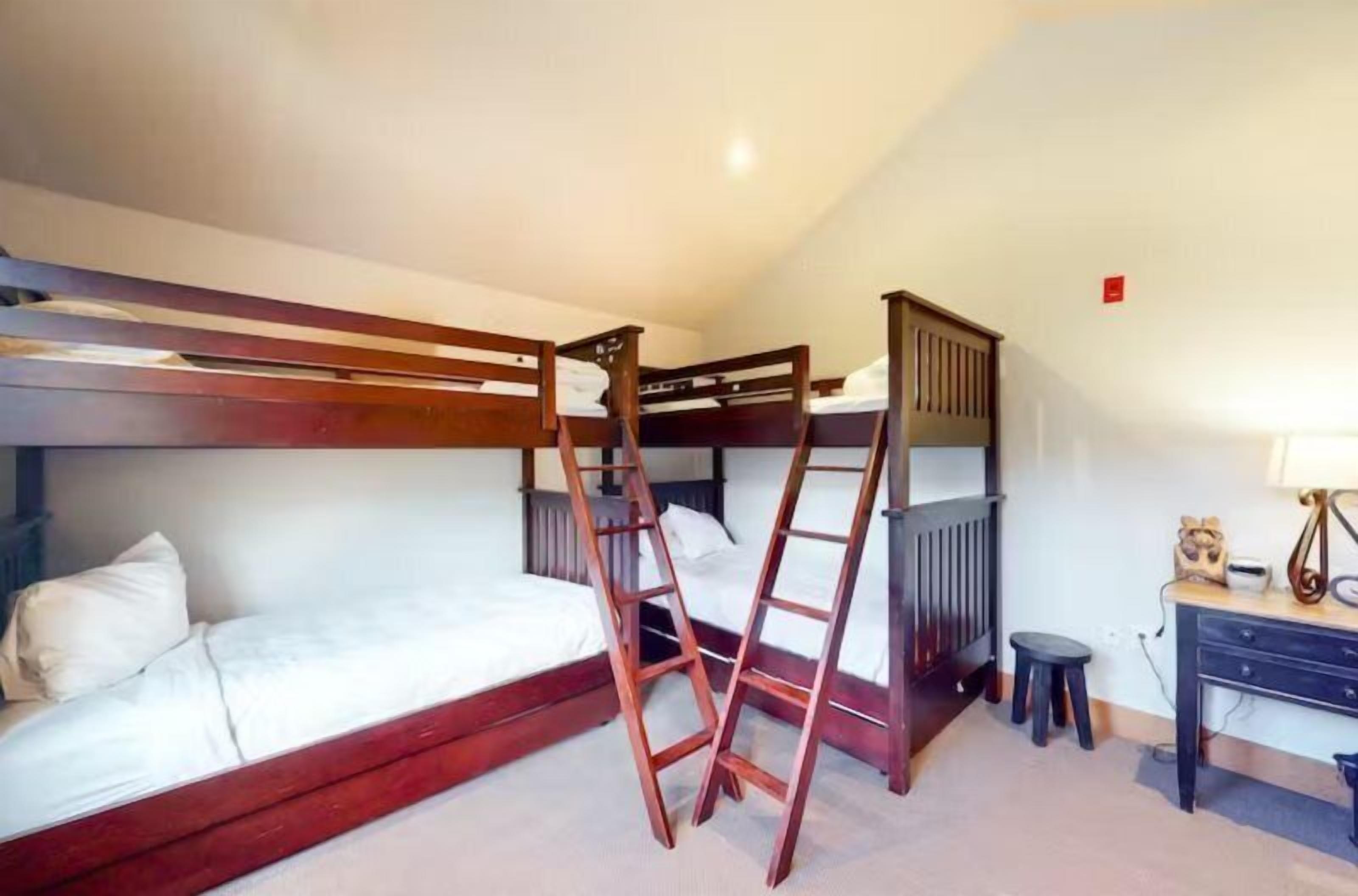 Une chambre avec un lit superposé, une échelle en bois, un bureau et une chaise.