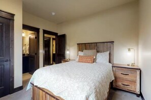 A bedroom with a large bed, wooden headboard, two bedside tables with lamps, and a dark wooden door. - River Run Townhomes - 3 Bedroom - Walk to Slopes! (Keystone)