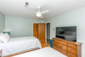 A bedroom with two beds, a ceiling fan, a television, and a wooden dresser.
