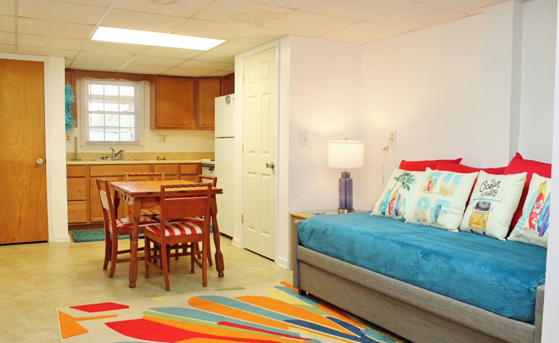 Un espacio habitable compacto con kitchenette, comedor y dormitorio con sofá y almohadones de colores.