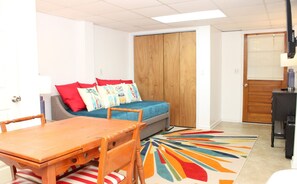 A compact living space with a wooden table, a sofa with colorful cushions, a small desk, and a vibrant rug. - The Knotty Hooker - Classic 4BR Soundfront Home - Pet Friendly! (Surf City)