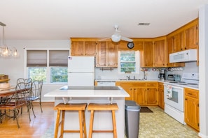A kitchen with wooden cabinets, a white refrigerator, a microwave, a stove, and a large island with stools.