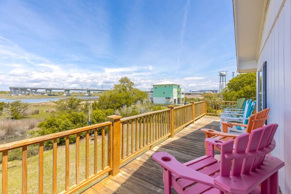 A wooden deck with a railing, pink chairs, and a view of a bridge and water. - The Knotty Hooker - Classic 4BR Soundfront Home - Pet Friendly! (Surf City)