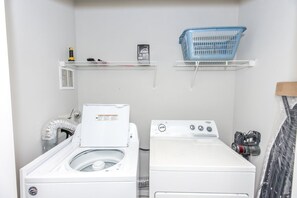 A laundry room with two washing machines, a blue laundry basket, and a shelf with cleaning supplies. - Shore Is Nice - 4BR Townhouse with Easy Beach Access! Pet Friendly! (Surf City)