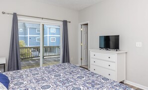 A bedroom with a bed, a dresser, a television, and a sliding glass door leading to a balcony.