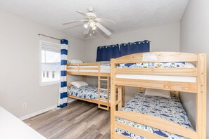 A room with three bunk beds, a ceiling fan, a window with curtains, and a view of buildings outside. - Shore Is Nice - 4BR Townhouse with Easy Beach Access! Pet Friendly! (Surf City)