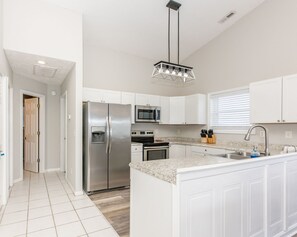 A modern kitchen with white cabinetry, stainless steel appliances, a granite countertop, and a pendant light.