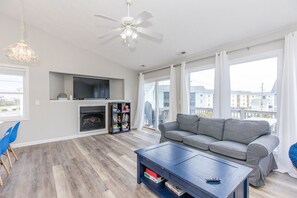 A modern living room with a grey sofa, a flat-screen TV, a fireplace, and a balcony with a view of buildings.