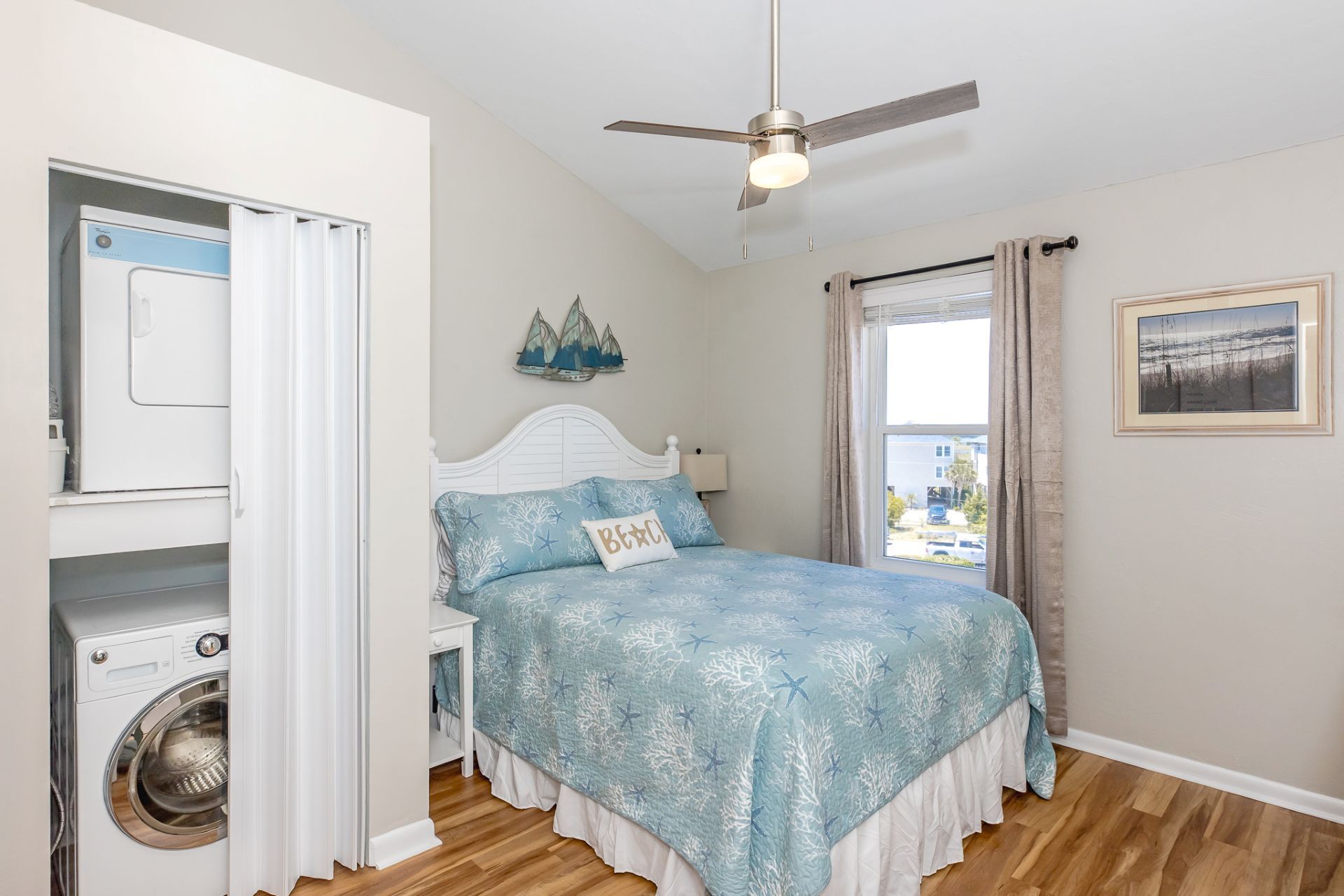 Une chambre à coucher avec un lit, un ventilateur de plafond, une fenêtre avec des rideaux et un lave-linge.