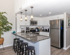 Cozinha moderna com ilha central, eletrodomésticos de aço inoxidável e iluminação pendente.