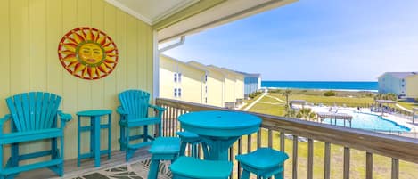 A balcony with turquoise chairs and tables, a sun decoration, and a view of the beach and pool area.