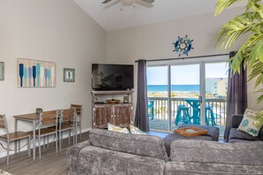 Ein Wohnzimmer mit Fernseher, Sitzgelegenheiten und Blick auf den Strand.