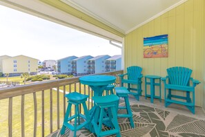 A balcony with turquoise chairs and stools, a patterned rug, and a painting of a bicycle on the wall. - The Sunny Surf - Top Floor Surf Condo - 2 BRs, 2 BA! (Surf City)
