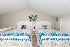 Quarto com duas camas, cada uma com cabeceira branca e edredom com padrão azul e branco.