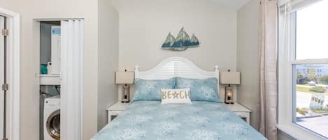 A bedroom with a bed, two bedside tables, a ceiling fan, a window with curtains, and a view of the outside.
