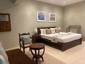 Ein Schlafzimmer mit einem Bett, Nachttischen, einem Sessel und zwei gerahmten Bildern an der Wand.