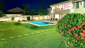 Una casa moderna con piscina, césped cuidado y un gran arbusto con flores rojas.