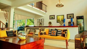 Un salón amplio con techo alto, una escalera de madera, un sofá amarillo con cojines estampados y un pez en un acuario de vidrio sobre una mesa de madera.