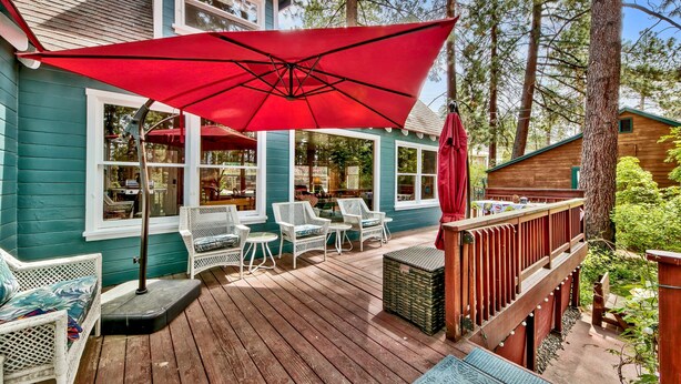 A wooden deck with outdoor furniture, a red umbrella, and a view of a house with multiple windows.