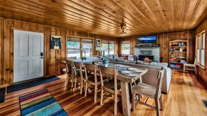 A wooden interior with a dining area, sofa, fireplace, and a TV.