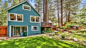 A two-story house with a deck, surrounded by a well-maintained garden and tall trees.