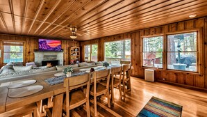 A wooden cabin interior with a large living area, fireplace, and large windows.