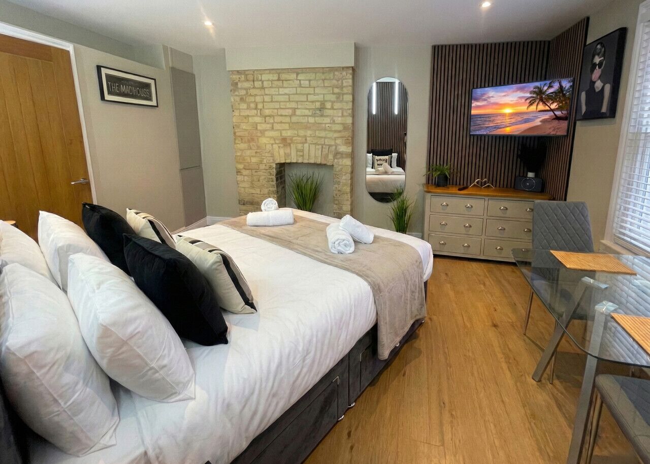 A modern hotel room with a large bed, a TV, a fireplace, and a dining area.