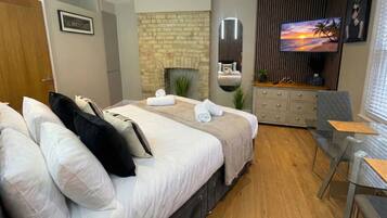 A modern hotel room with a large bed, a TV, a fireplace, and a dining area.