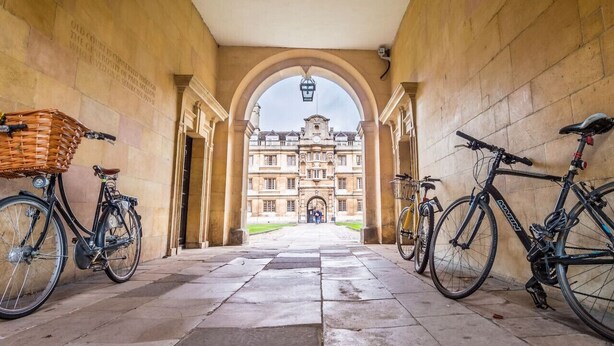 A corridor with bicycles parked on either side, leading to a historic building with an arched entrance. - Modern en-suite Studio in the Heart of Mill Road (Cambridge)