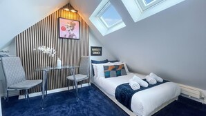 A modern bedroom with a sloped ceiling, a bed with a blue and white duvet, a small table with a chair, and a picture on the wall. - Modern ensuite Studio Retreat off Vibrant Mill Rd (Cambridge)