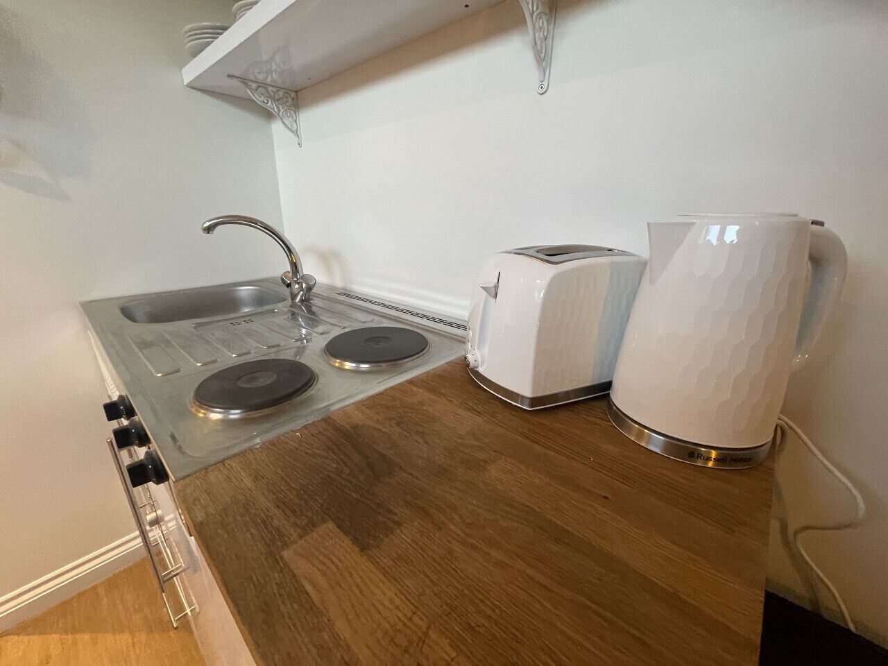 A kitchen with a stove, two white toasters, and a white kettle on a wooden countertop.