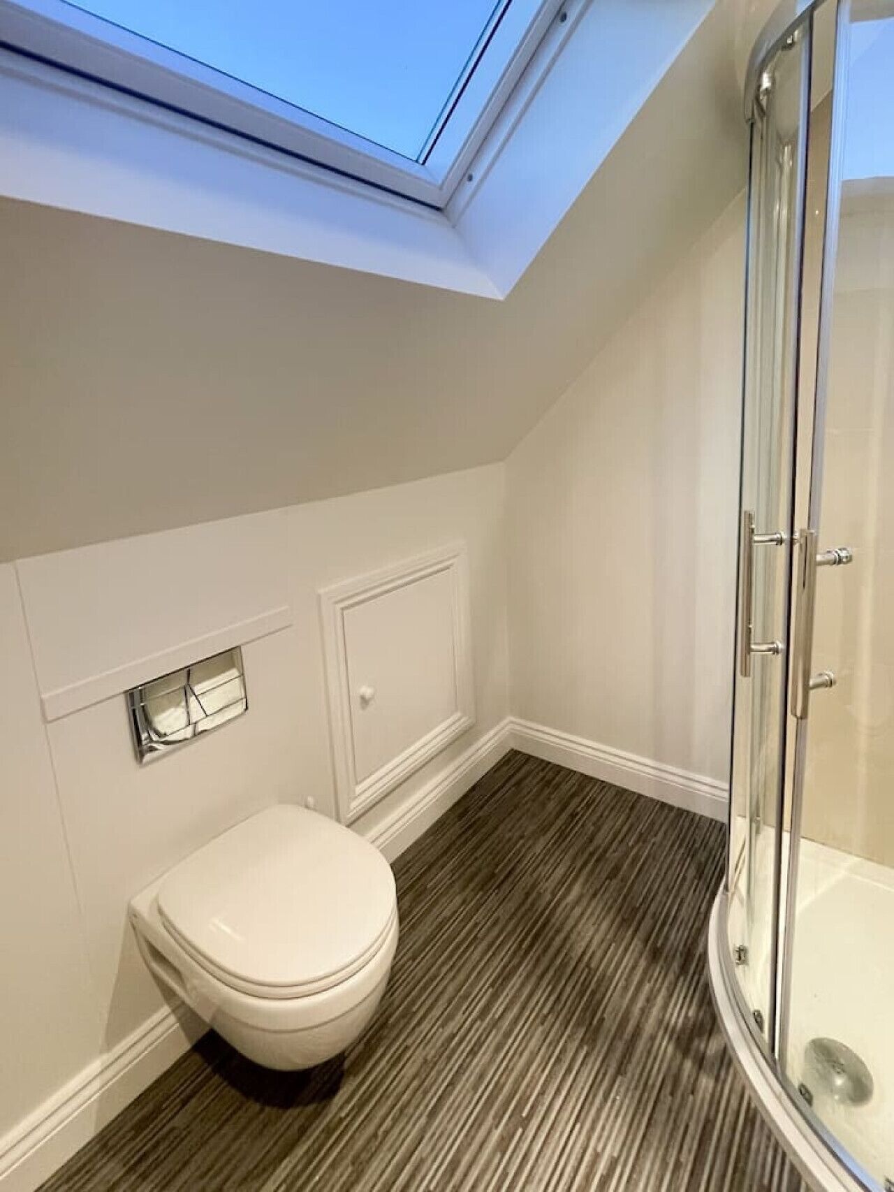 A modern bathroom with a skylight, a toilet, a shower enclosure, and a patterned floor.