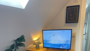A room with a dark blue dresser, a television on top displaying a seascape, a potted plant, and a framed artwork on the wall. - Modern ensuite Studio Retreat off Vibrant Mill Rd (Cambridge)