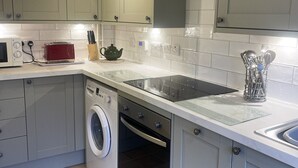 Une cuisine moderne avec des meubles gris, un four encastré, un lave-linge et un four à micro-ondes.