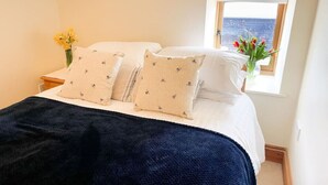 Ein ordentlich bezogenes Bett mit einer dunkelblauen Decke, zwei Kissen mit einem kleinen Muster und einem Blumenstrauß auf dem Nachttisch.