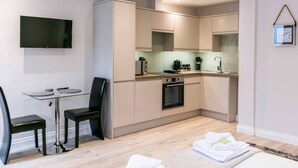 A modern kitchen with a flat-screen TV, a dining area with a glass table and chairs, and a small seating area with a sofa. - Modern Studio - just off Mill Rd nr train station (Cambridge)