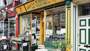 A storefront with a sign reading "Arjuna Wholefoods 100% Vegetarian" and a visible outdoor seating area with a table and chairs.